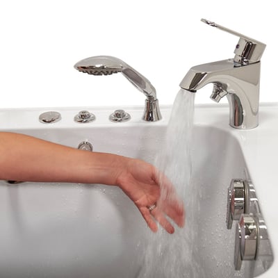 Person testing warm water temperature from chrome faucet filling an Ella walk-in bathtub with handheld showerhead and jet controls