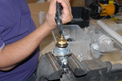 Technician using a wrench to tighten a brass thermostatic control valve cartridge secured in a bench vise during walk-in tub assembly