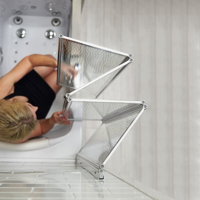 Tempered glass shower screen folded back in a concertina while a bather reclines in the walk in tub.