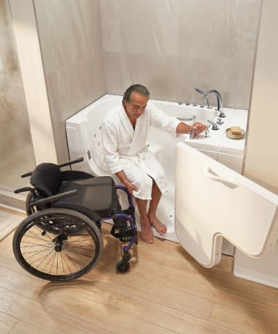 Personne en peignoir blanc effectuant un transfert dans la baignoire à porte Ella Transfer30, avec la porte à ouverture vers l’extérieur ouverte à proximité